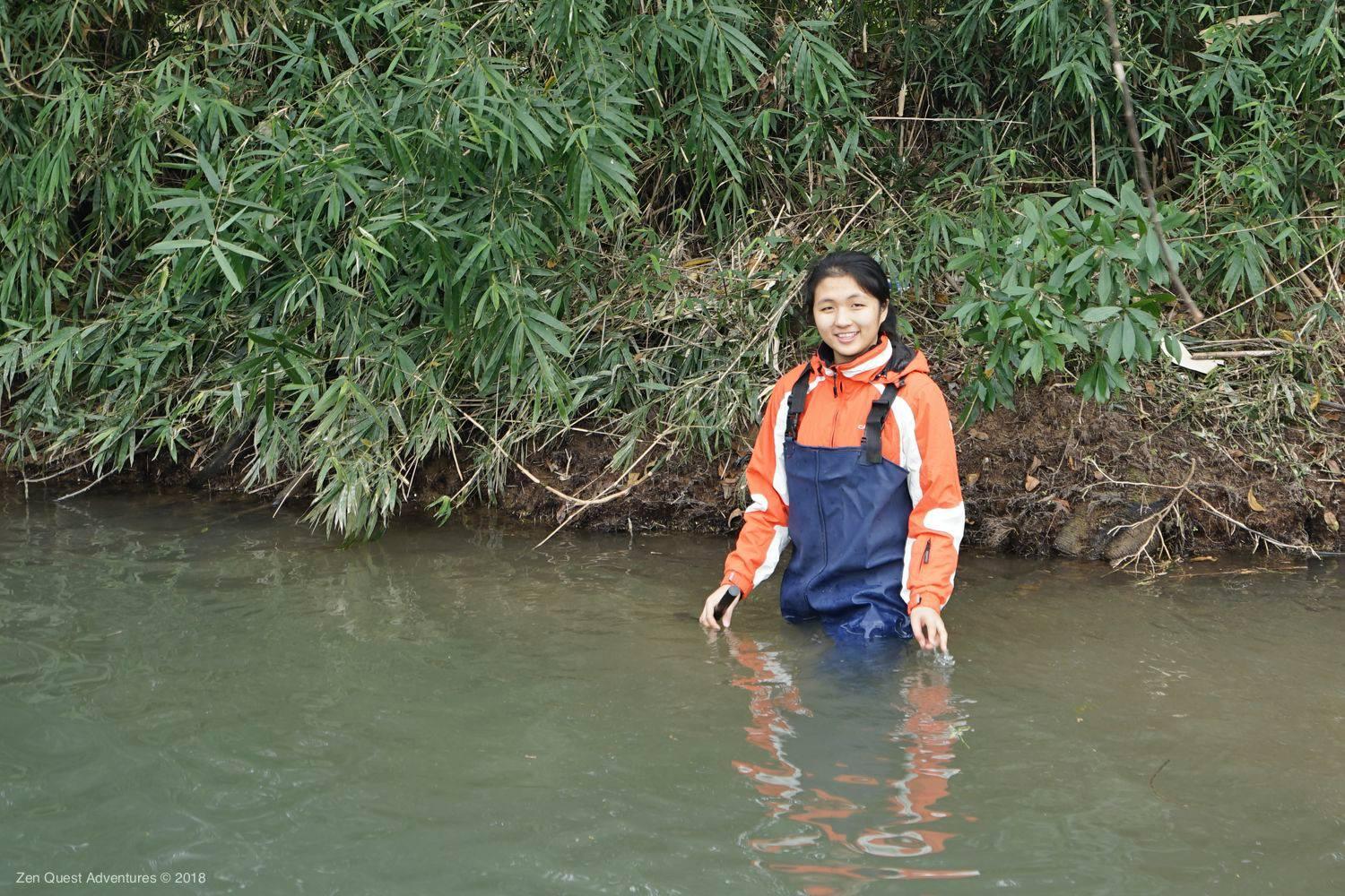 River studies, girl in river with fishing waders and poll